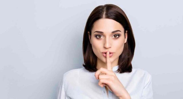 TS, secreto profesional, abogados, intermediarios, mecanismos transfronterizos, obligación de informar, DAC 6, suspensión cautelar, art. 45.4.b), RGAT TS, secreto profesional, abogados, intermediarios, mecanismos transfronterizos, obligación de informar, DAC 6, suspensión cautelar, art. 45.4.b), RGAT. Primer plano de una mujer joven que mira de frente pide silencio con el dedo sobre la boca