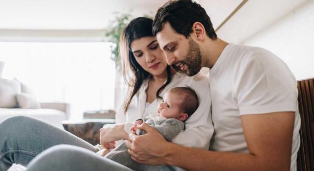 No existe discriminación por negar al padre la deducción por maternidad en el IRPF. Imagen de un padre con su bebé a brazos y la mama del bebé a su lado