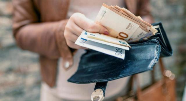 Modificación del plazo de ingreso en período voluntario de los recibos del IAE 2024 para cuotas nacionales y provinciales. Imagen de las manos de una mujer sacando billetes de su cartera